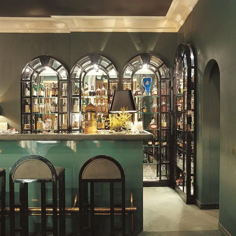 Un bar arredato su misura: bancone verde, sgabelli e vetrine ad arco piene di bottiglie